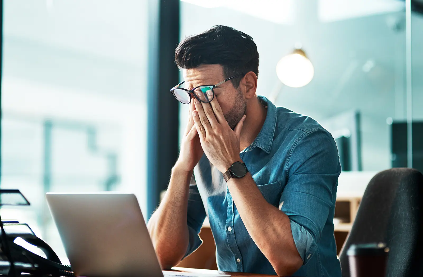 Man sitting at a desk with hands on his face while reviewing a website on his laptop.